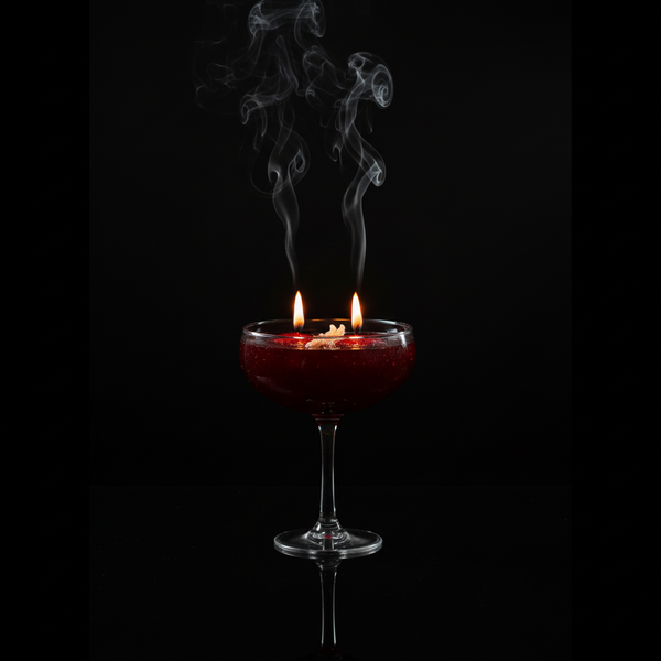 Luxury candle with two lit wicks and smoke on black reflective surface